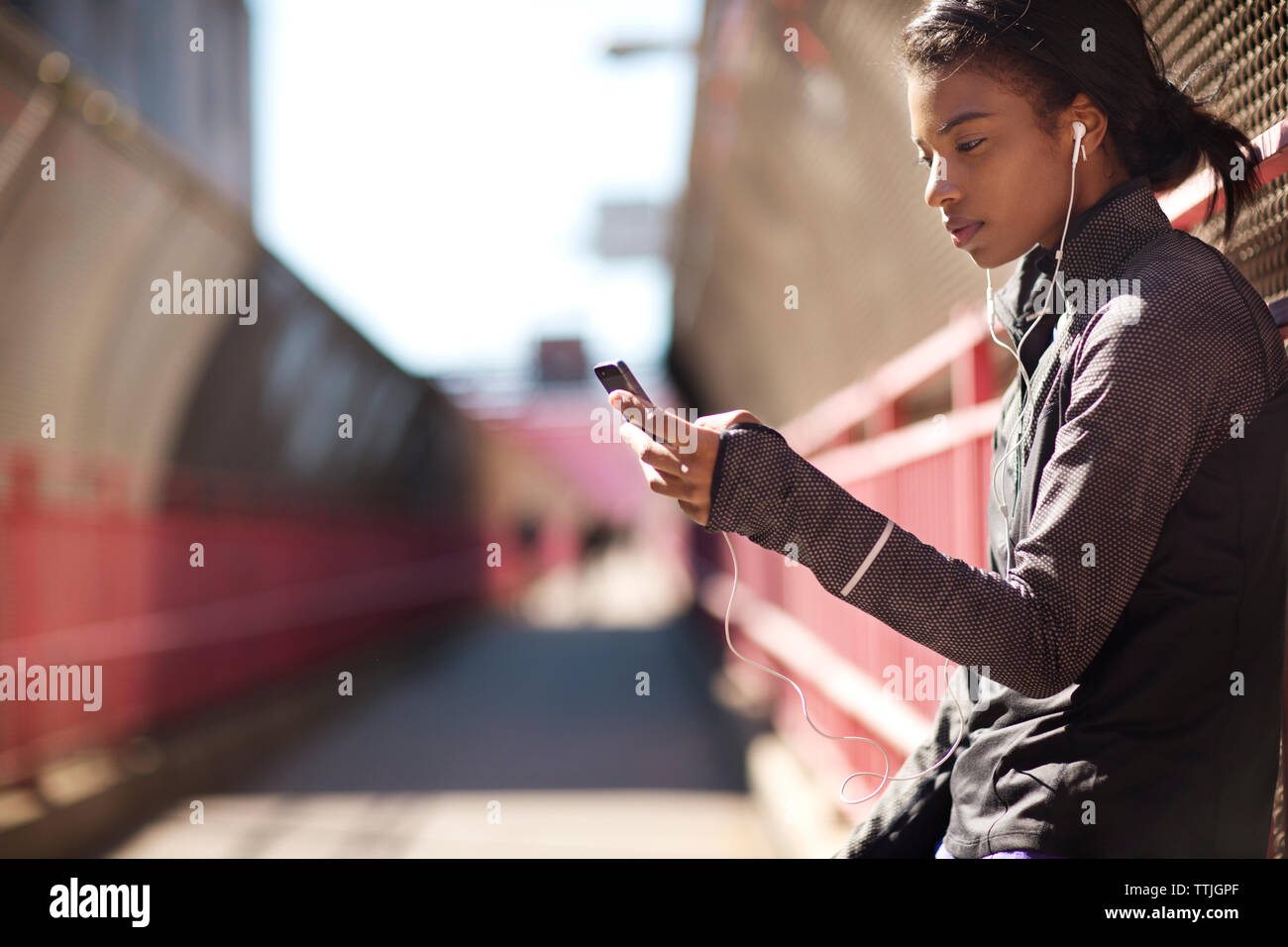 Vista laterale della donna ascoltare musica mentre appoggiata sulla recinzione al Williamsburg Bridge passaggio pedonale Foto Stock