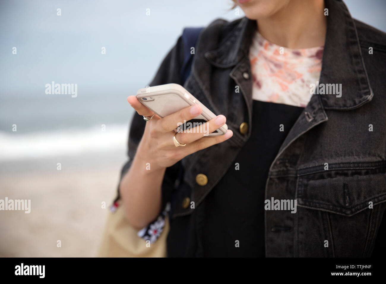 Sezione mediana della donna utilizzando smart phone mentre si sta in piedi in spiaggia Foto Stock