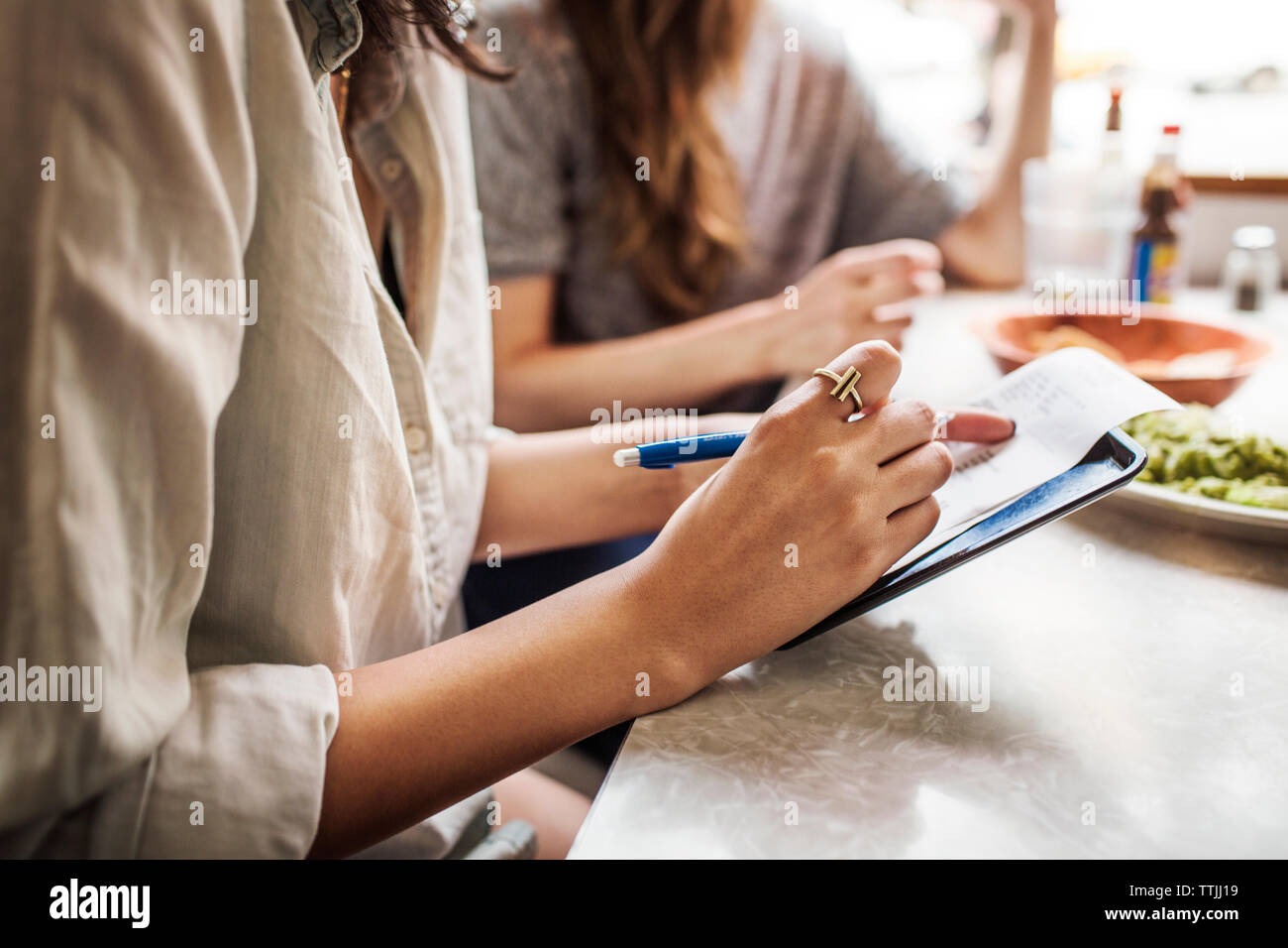 Sezione mediana della donna la scrittura sulla carta mentre si siede con gli amici nel ristorante Foto Stock