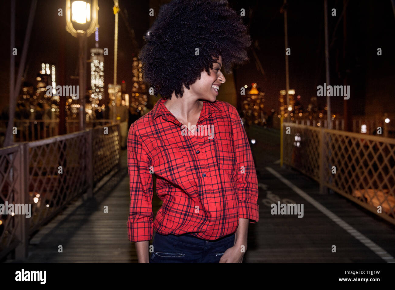 Donna sorridente che guarda lontano mentre si sta in piedi sul ponte di Brooklyn Foto Stock