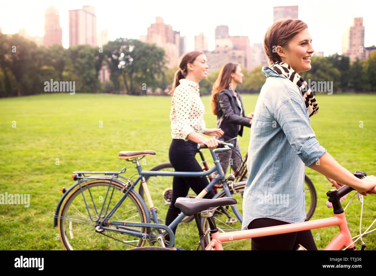 Le donne con le biciclette passeggiate sul campo nel parco contro la città Foto Stock