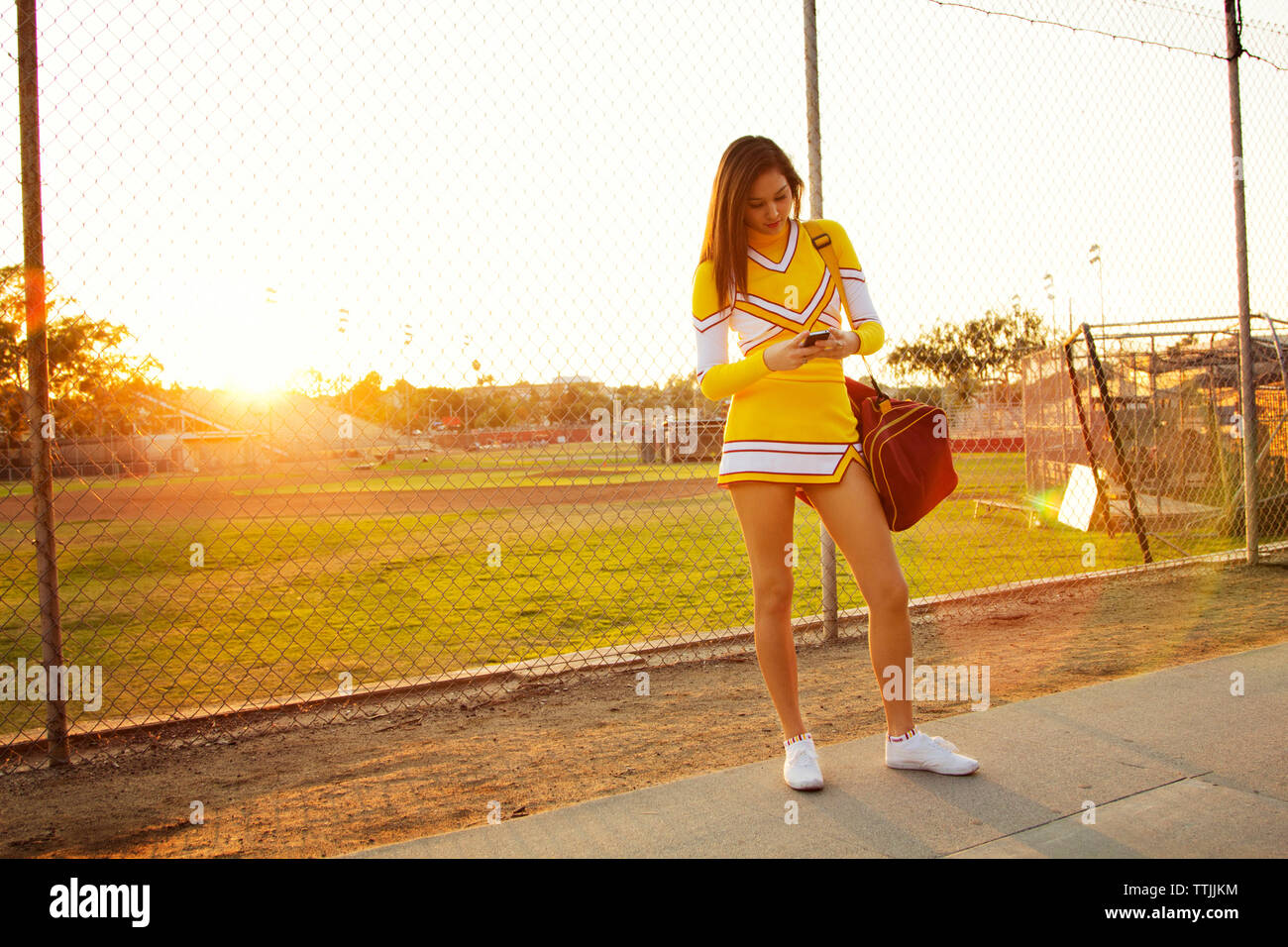 Donna che utilizza smart phone mentre si sta in piedi sul sentiero contro il campo di gioco Foto Stock