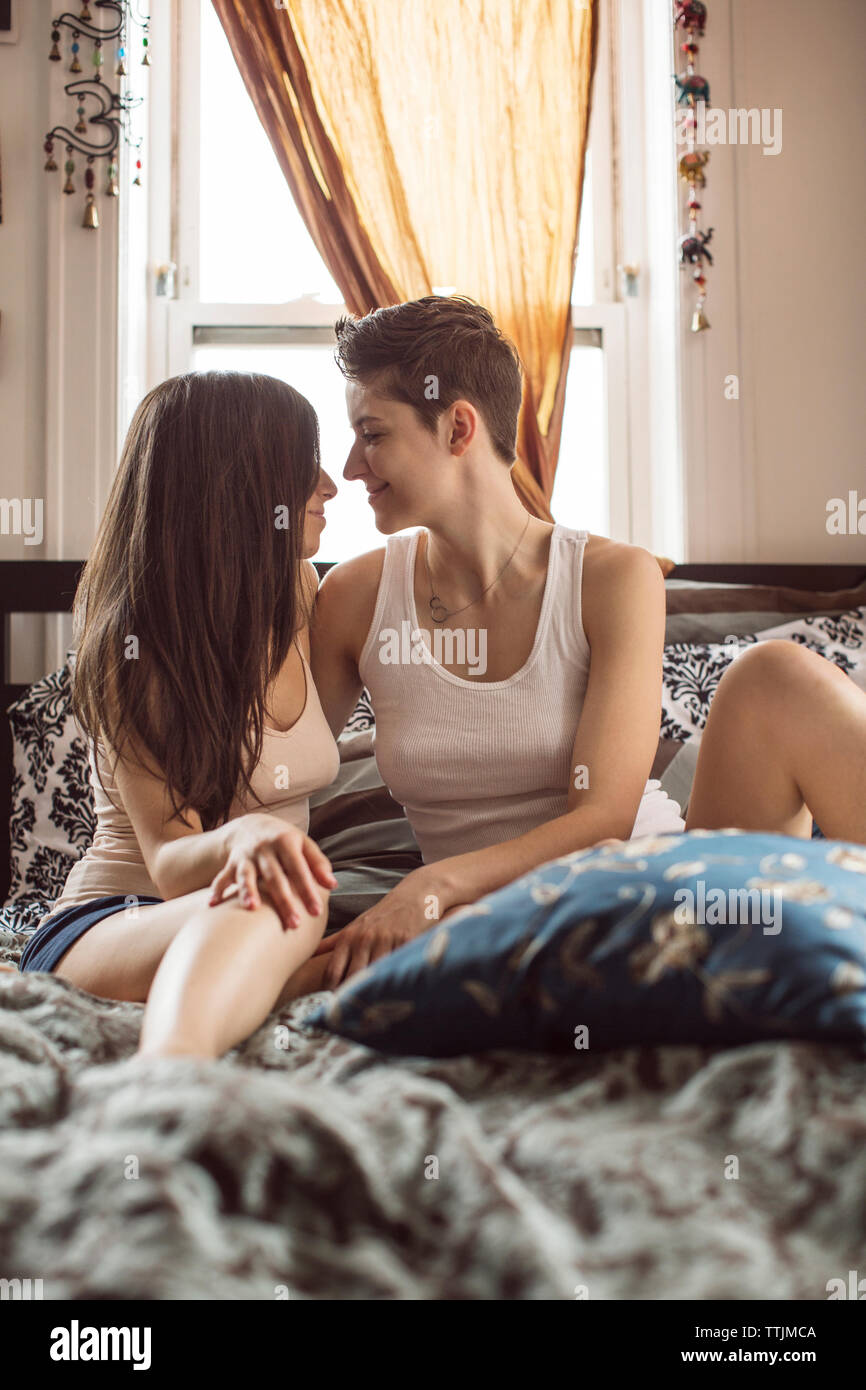 Lesbiche sorridente seduta sul letto di casa Foto Stock