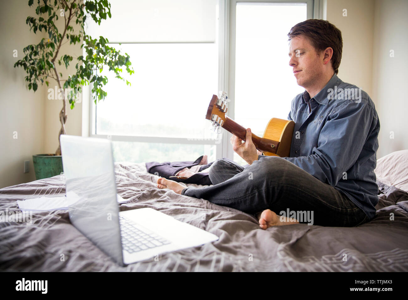Uomo che utilizza il computer portatile per imparare la chitarra a casa Foto Stock
