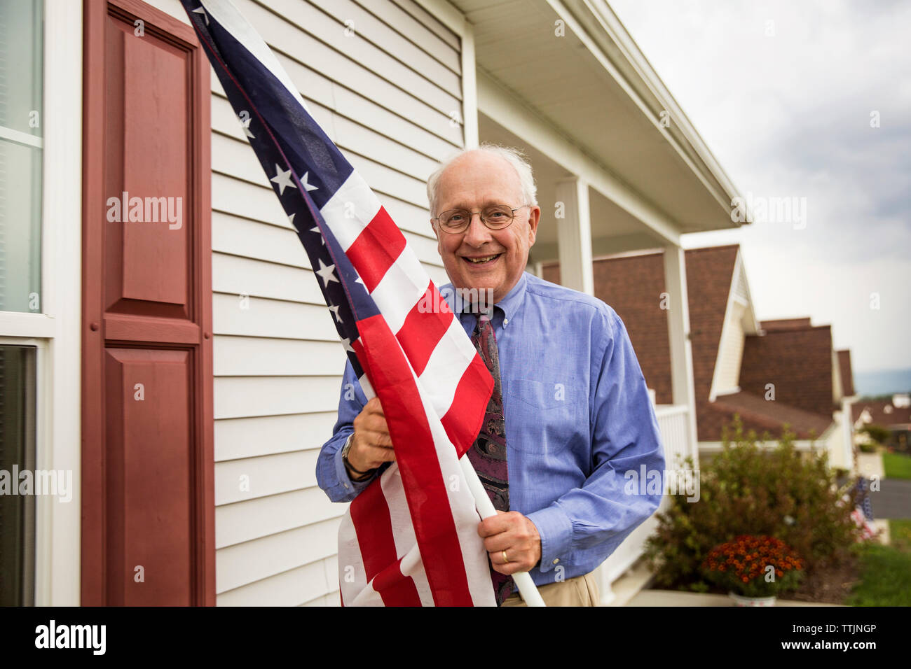 Ritratto di senior uomo con bandiera americana mentre in piedi contro la casa Foto Stock