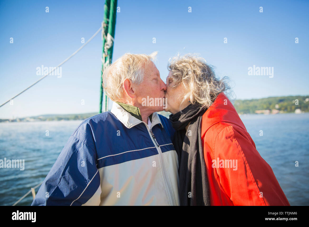 Romantico coppia senior baciare in barca sul mare contro il cielo chiaro Foto Stock