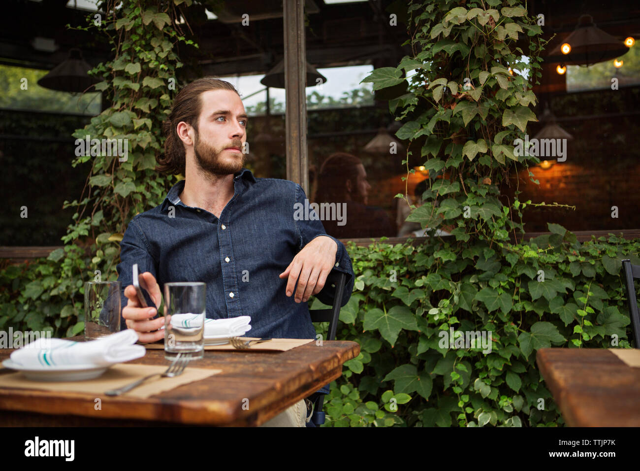 Considerato l uomo azienda smart phone mentre seduti al cafè sul marciapiede Foto Stock