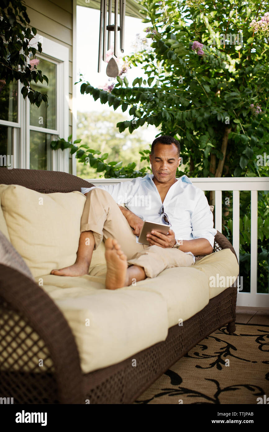 Uomo che utilizza computer tavoletta mentre vi rilassate sul divano in veranda Foto Stock