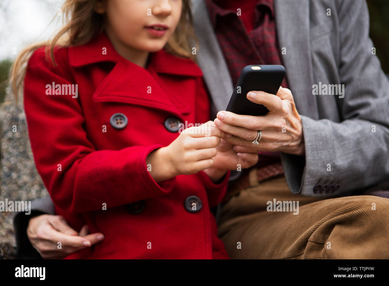 Sezione mediana della famiglia utilizzando il telefono cellulare mentre è seduto su un banco di lavoro in posizione di parcheggio Foto Stock