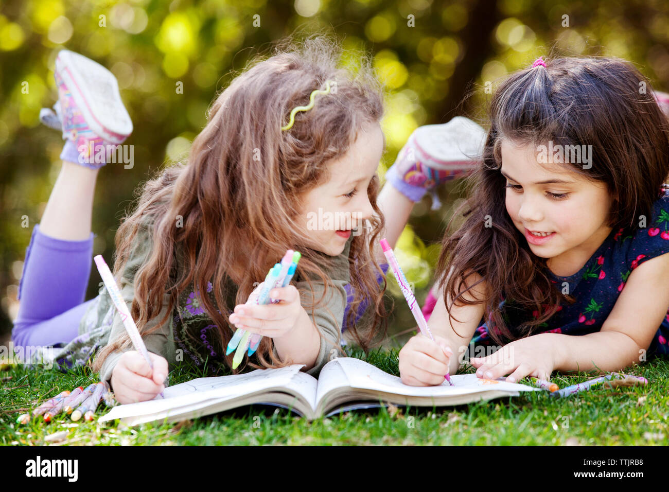 Ragazze disegno sul libro da colorare mentre giaceva sul campo Foto Stock