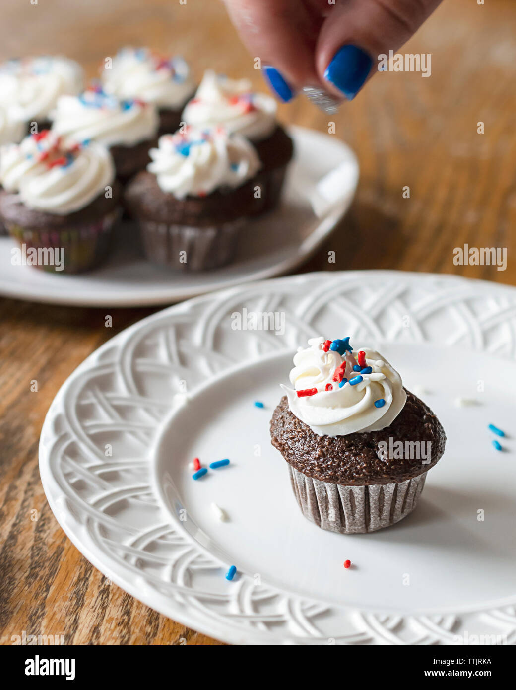 Il cioccolato mini cupcake sulla piastra bianca decorata con rosso, bianco e blu spruzza. Dita con motion blurr in foto. Decorate aggiuntivi Foto Stock