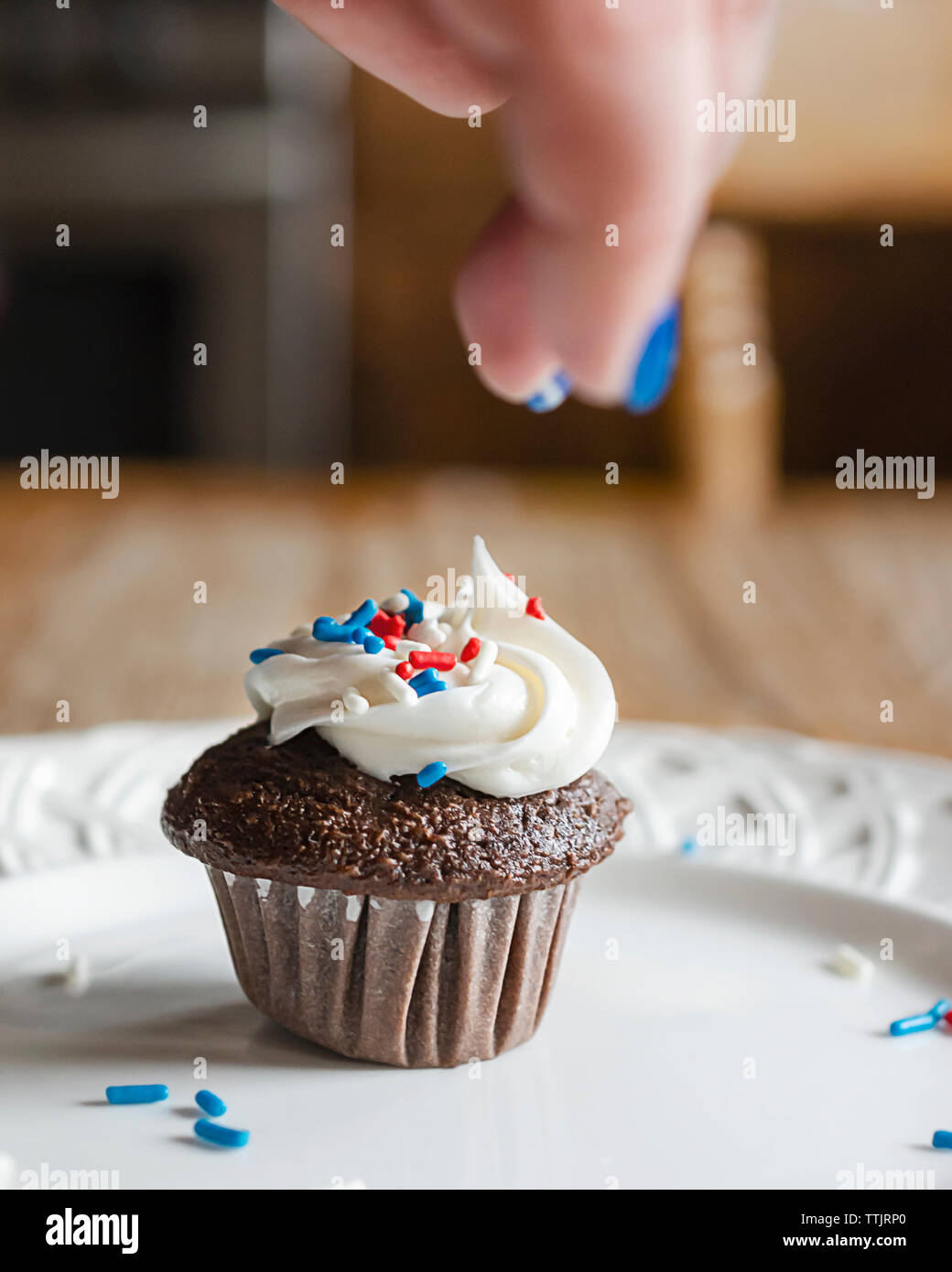 Il cioccolato mini cupcake su una piastra bianca è irrorato con rosso, bianco e blu spruzza. Sfocata sopra mano gocciolamento spruzza. Foto Stock