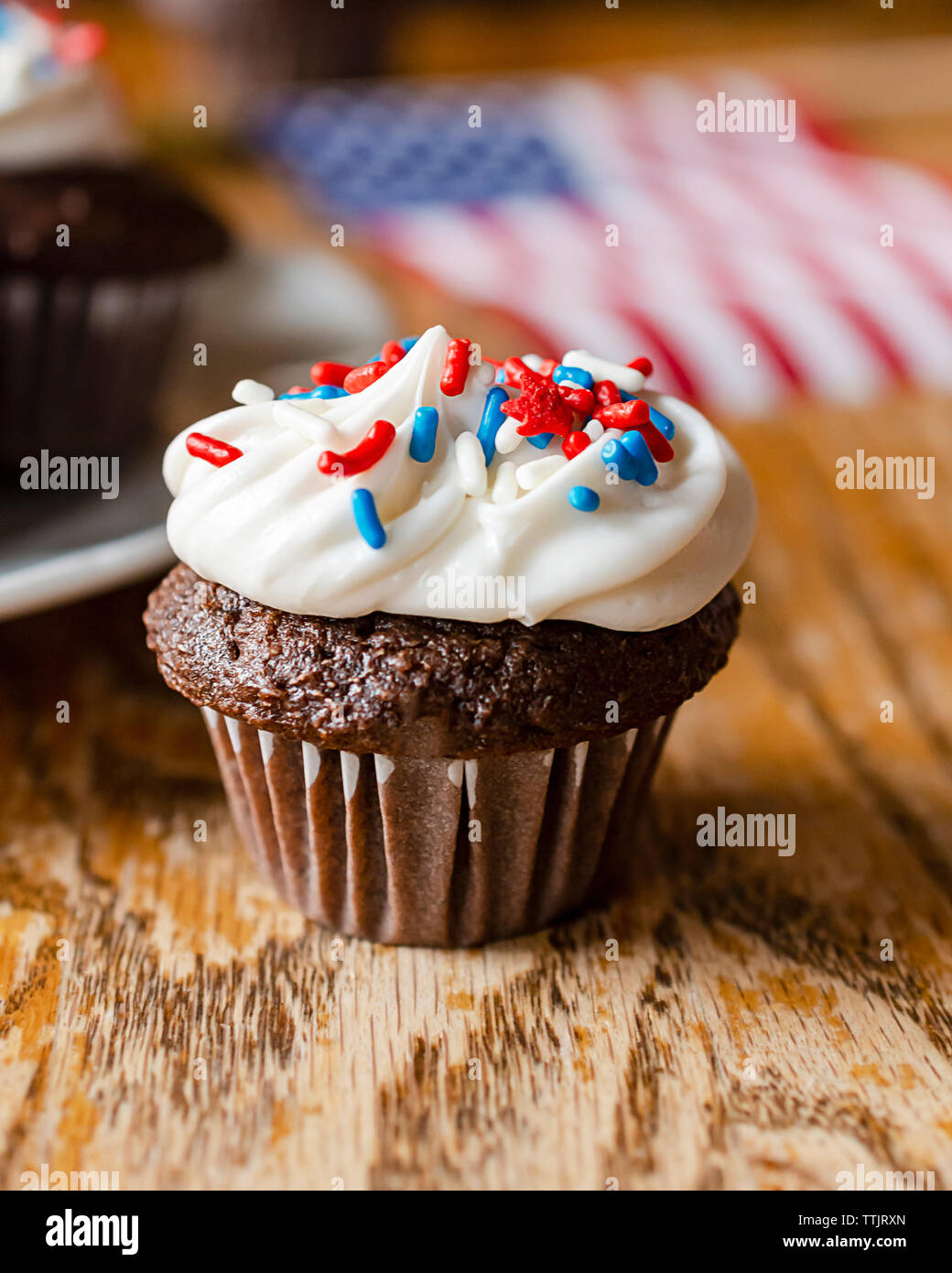 Close up di un mini cupcake al cioccolato con rosso, bianco e blu spruzza. Ulteriori tortine e noi bandiera sfumata in background. Un tavolo di legno. Foto Stock