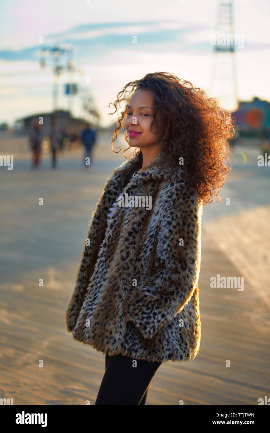 Donna sorridente con capelli ricci indossa pelliccia mentre in piedi a Coney Island Foto Stock