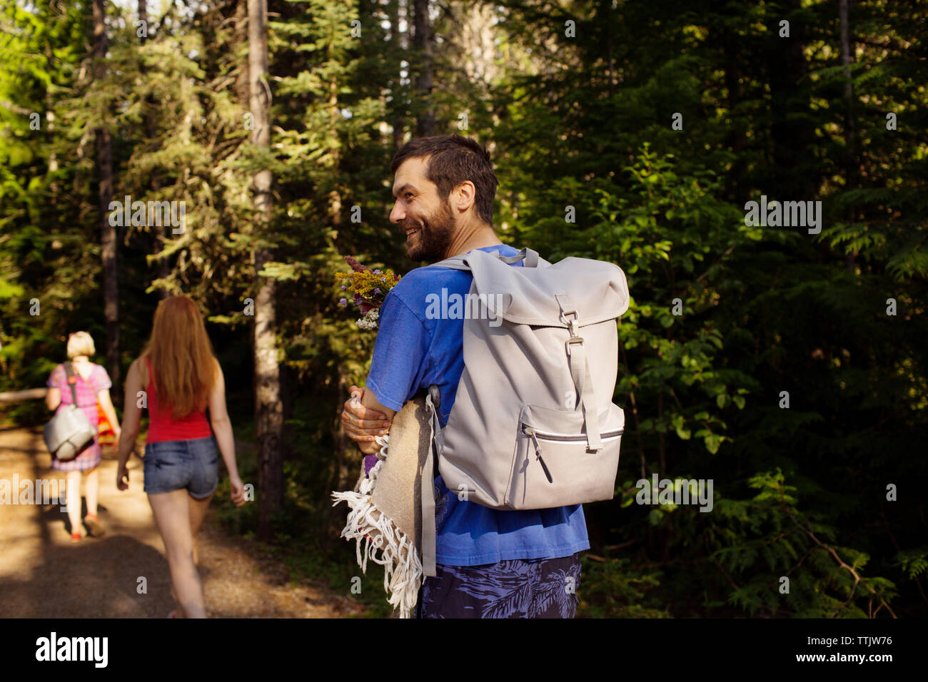 Uomo sorridente zaino porta a piedi con la madre e la sorella da alberi in foresta Foto Stock