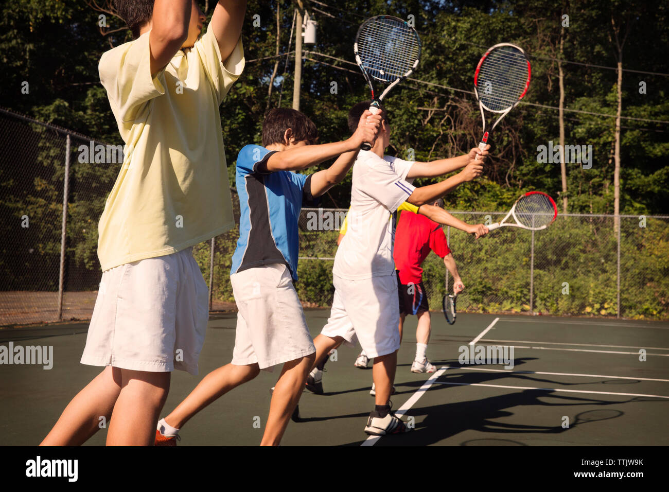 I giocatori in piedi in fila giocando a tennis contro il recinto a corte Foto Stock