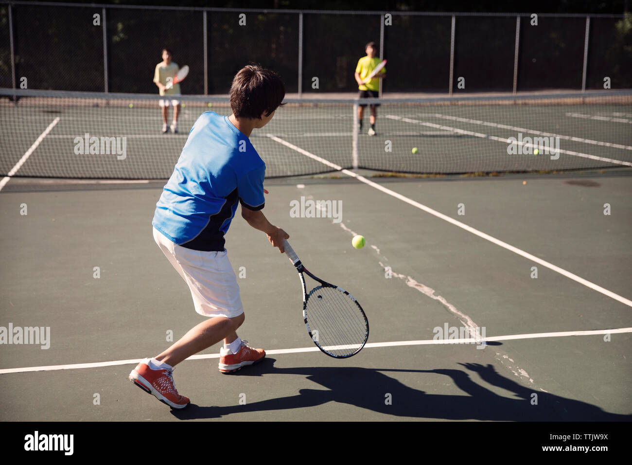Ragazzi giocare a tennis presso la Corte contro il recinto sul giorno di sole Foto Stock