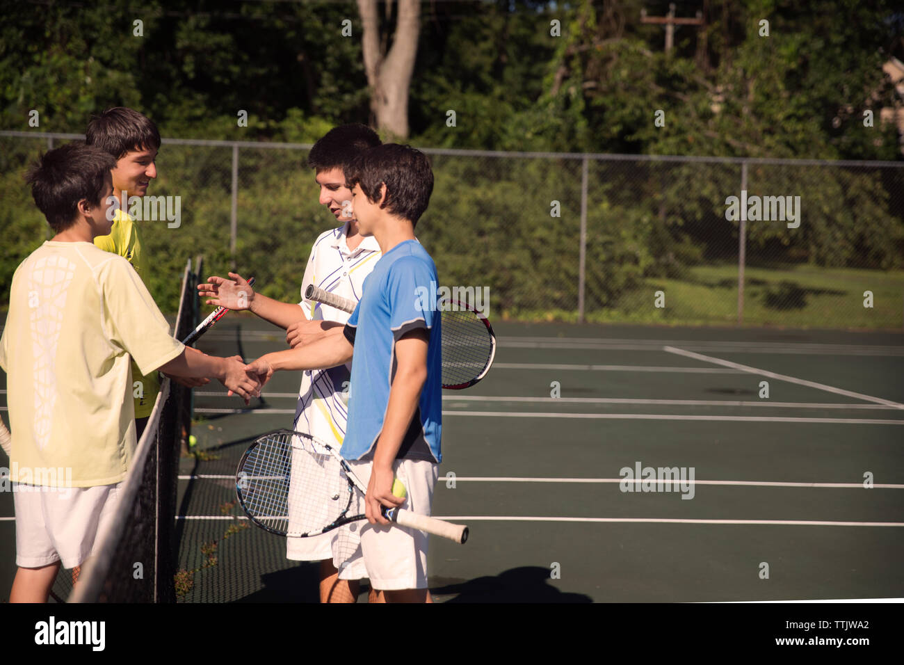 I giocatori si stringono la mano su net mentre si gioca a tennis a corte Foto Stock