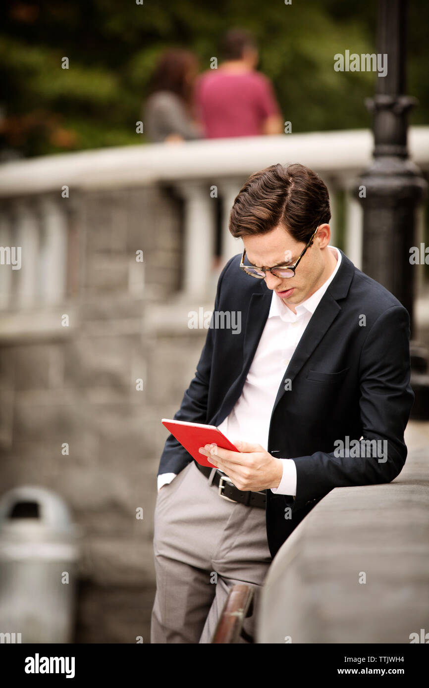 uomo d'affari che usa un tablet mentre si appoggia alle ringhiere Foto Stock