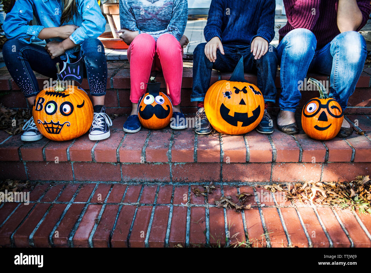 Sezione bassa della famiglia seduta con zucche decorate sulle fasi durante il periodo di Halloween Foto Stock