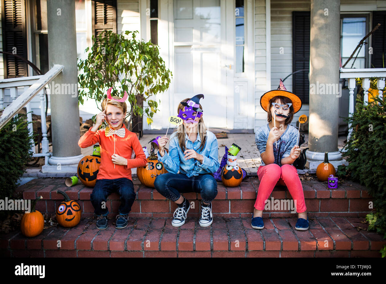 Felice fratelli azienda puntelli seduta con zucche decorate sulle fasi durante il periodo di Halloween Foto Stock