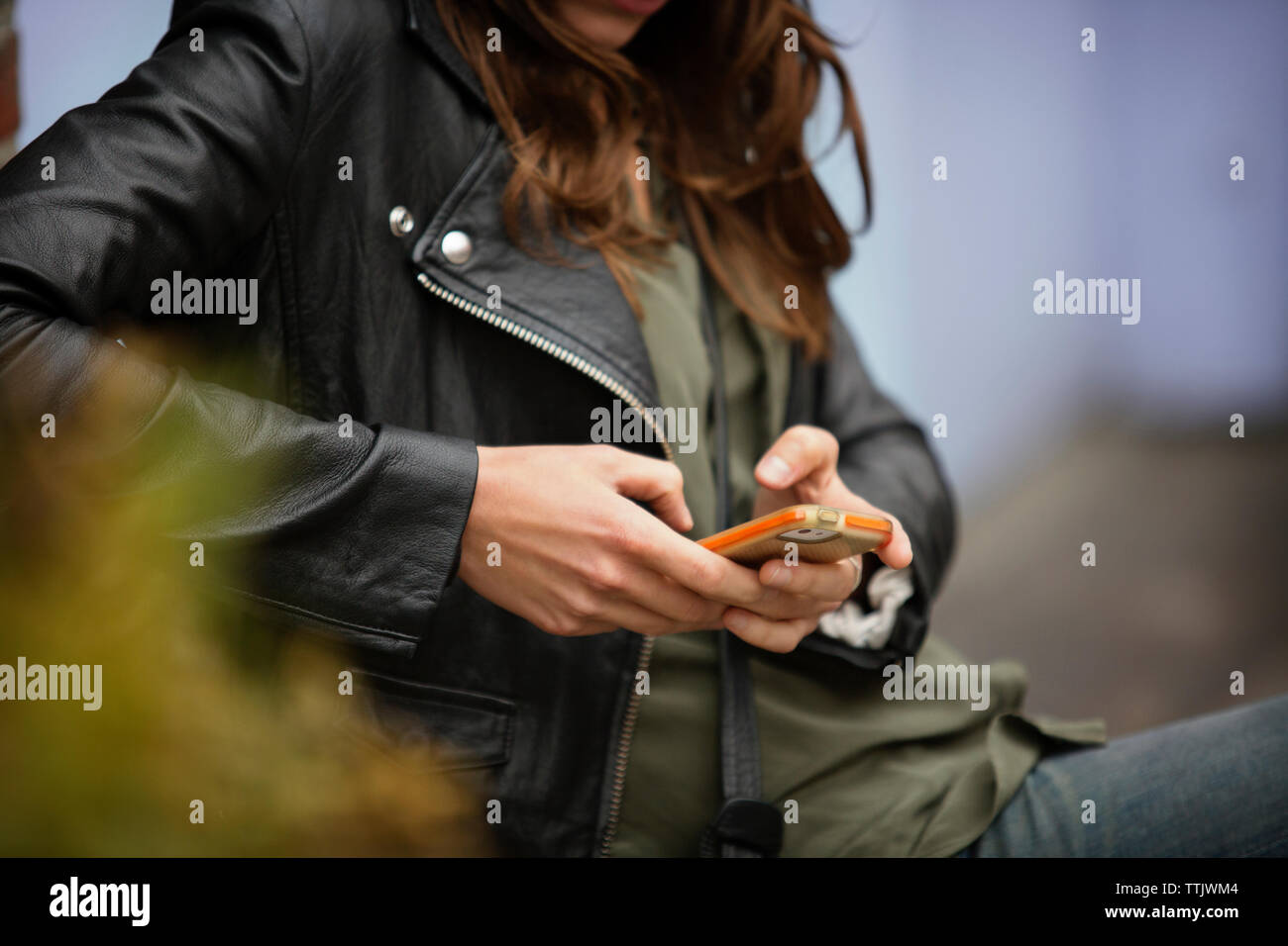 Sezione mediana della donna utilizzando il telefono cellulare mentre si riposa all'aperto Foto Stock
