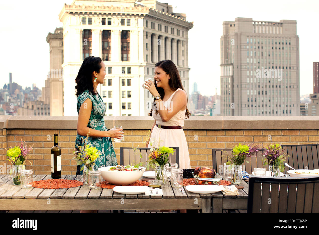 Happy amici avente il vino in piedi dalla tabella degli alimenti a costruire in terrazza in città Foto Stock