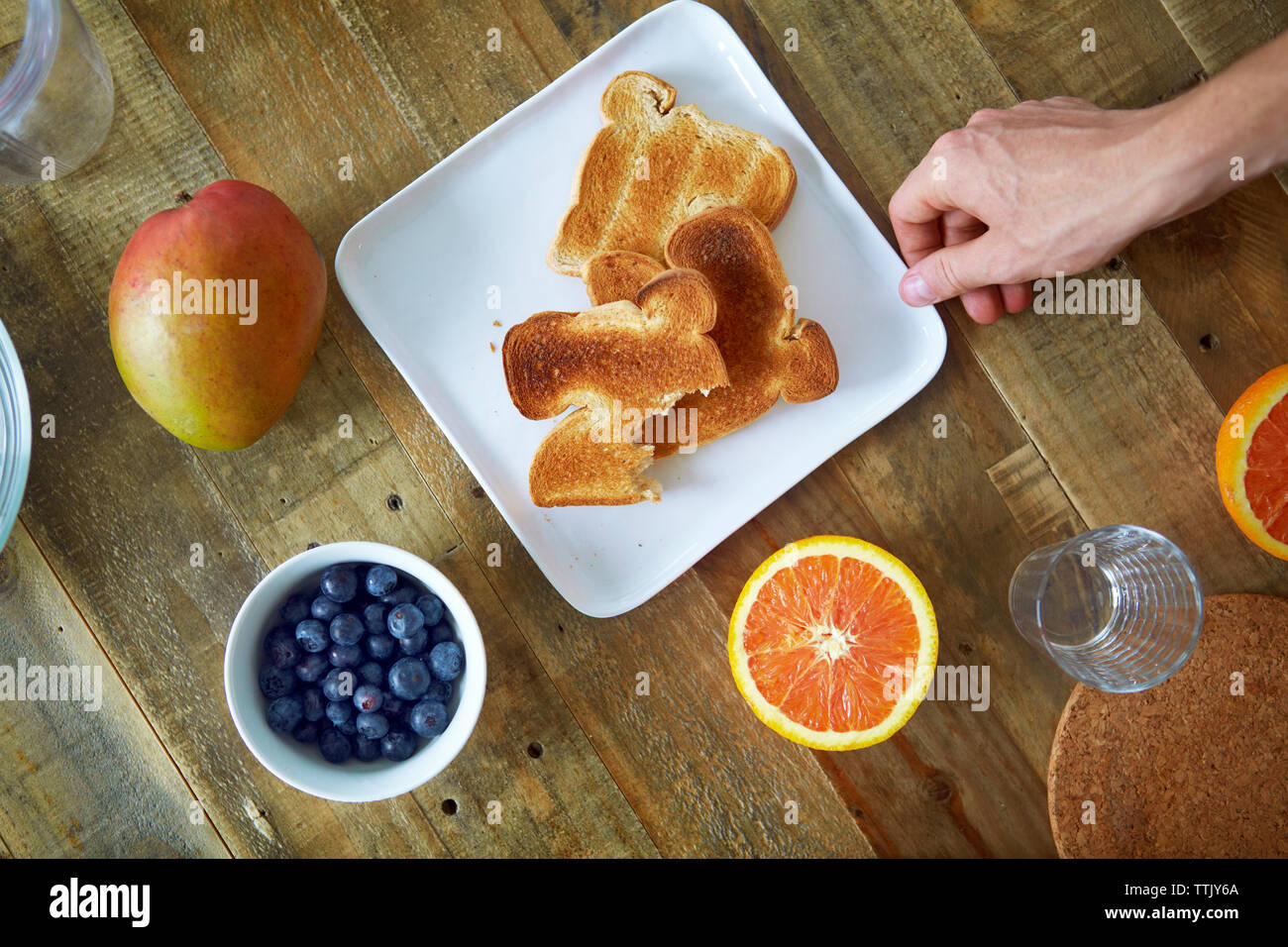 Immagine ritagliata della mano che tiene il pane tostato in piastra sul tavolo di legno Foto Stock