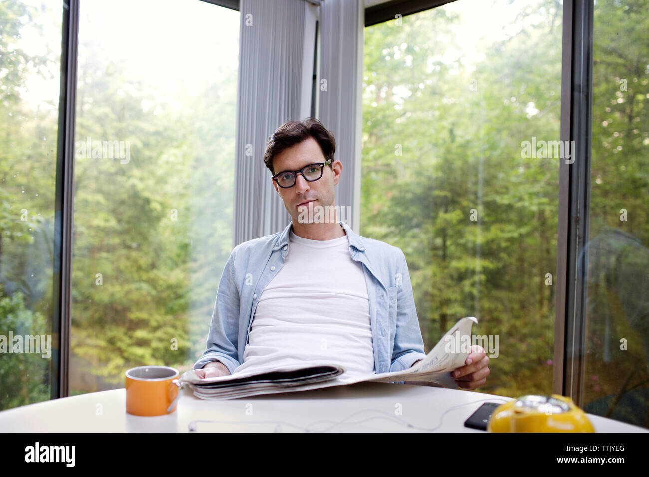 Ritratto di uomo con giornale mentre avente il tè al tavolo contro la finestra Foto Stock