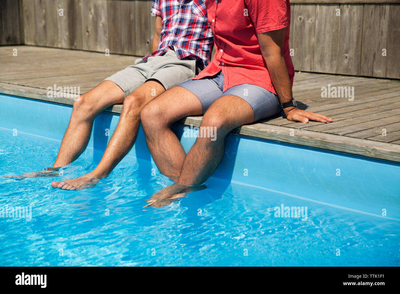 Sezione bassa della coppia omosessuale rilassarsi sul bordo della piscina Foto Stock