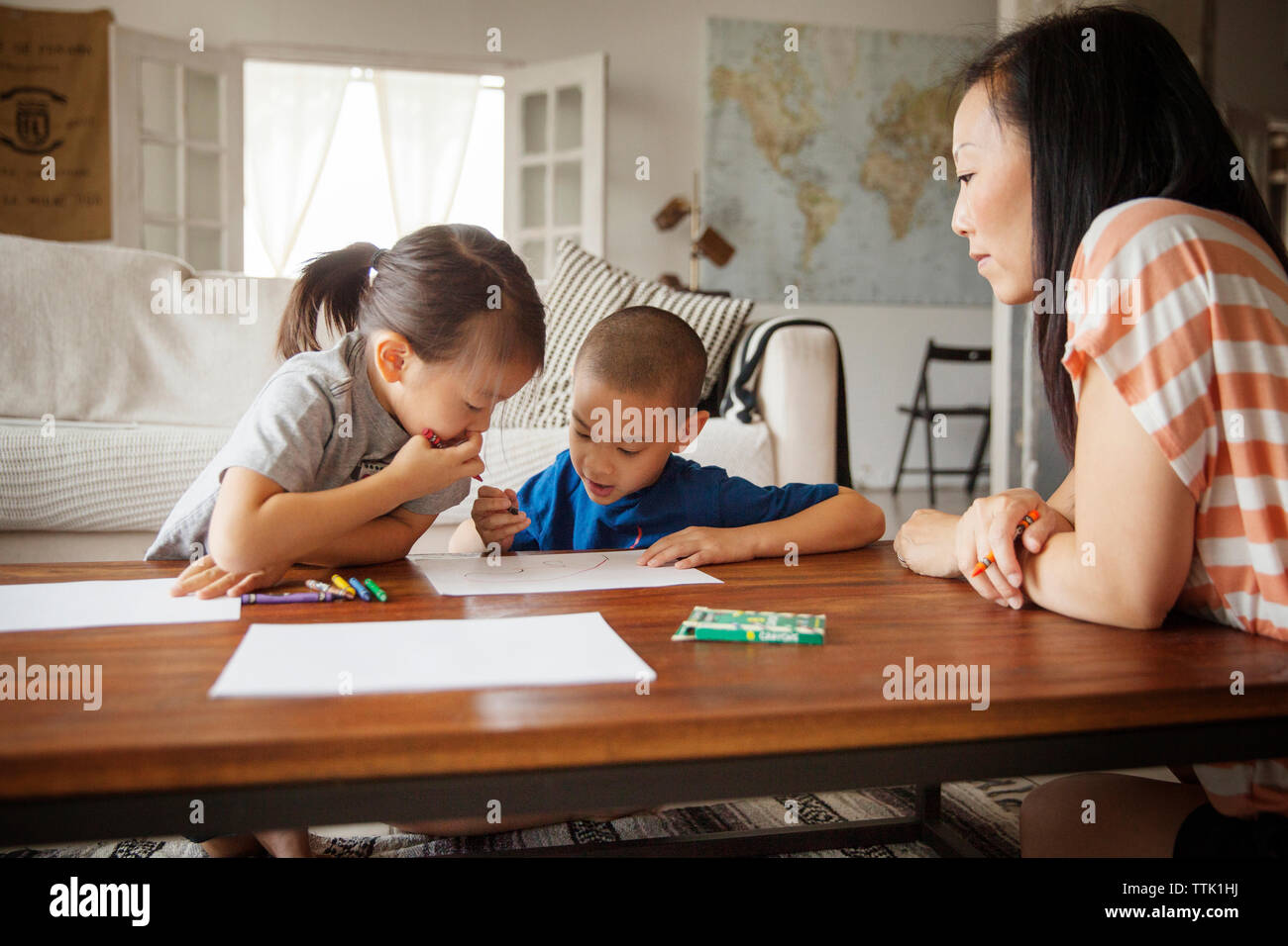 Madre guardando i bambini disegno sulla tavola in soggiorno Foto Stock