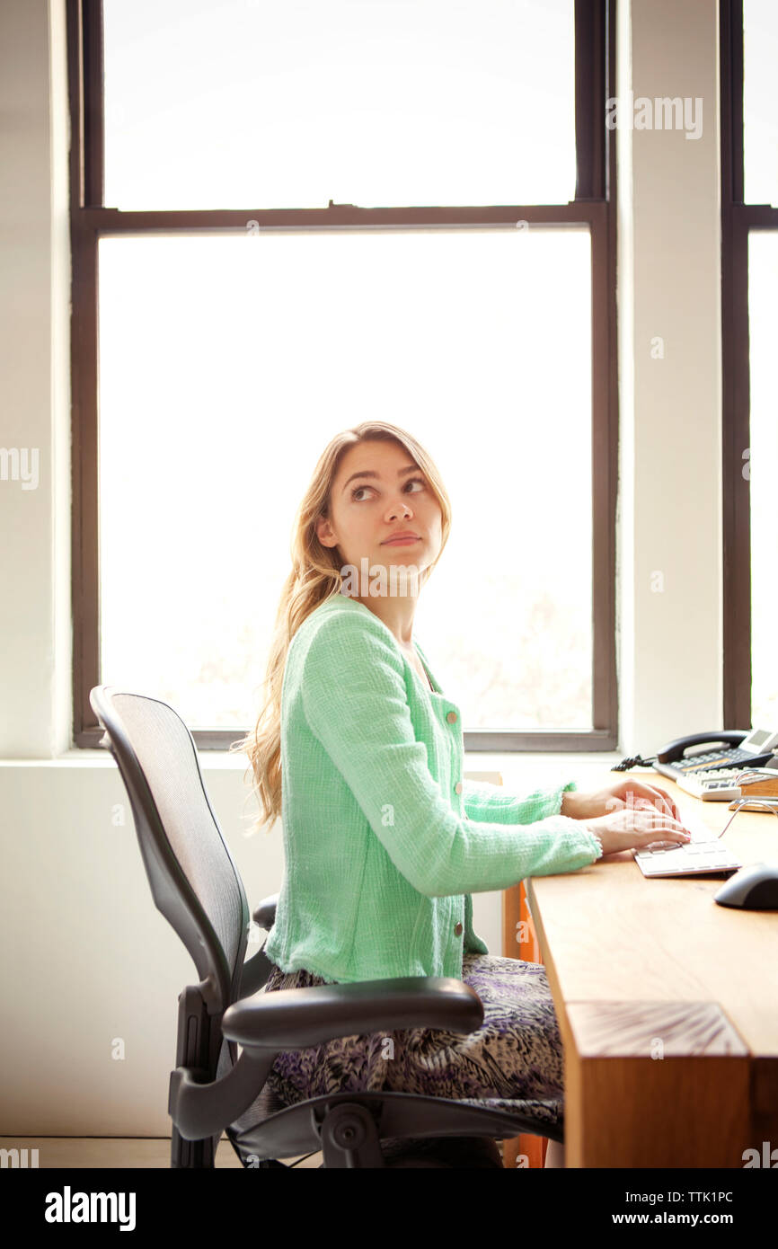 donna d'affari seduta alla scrivania accanto alla finestra Foto Stock