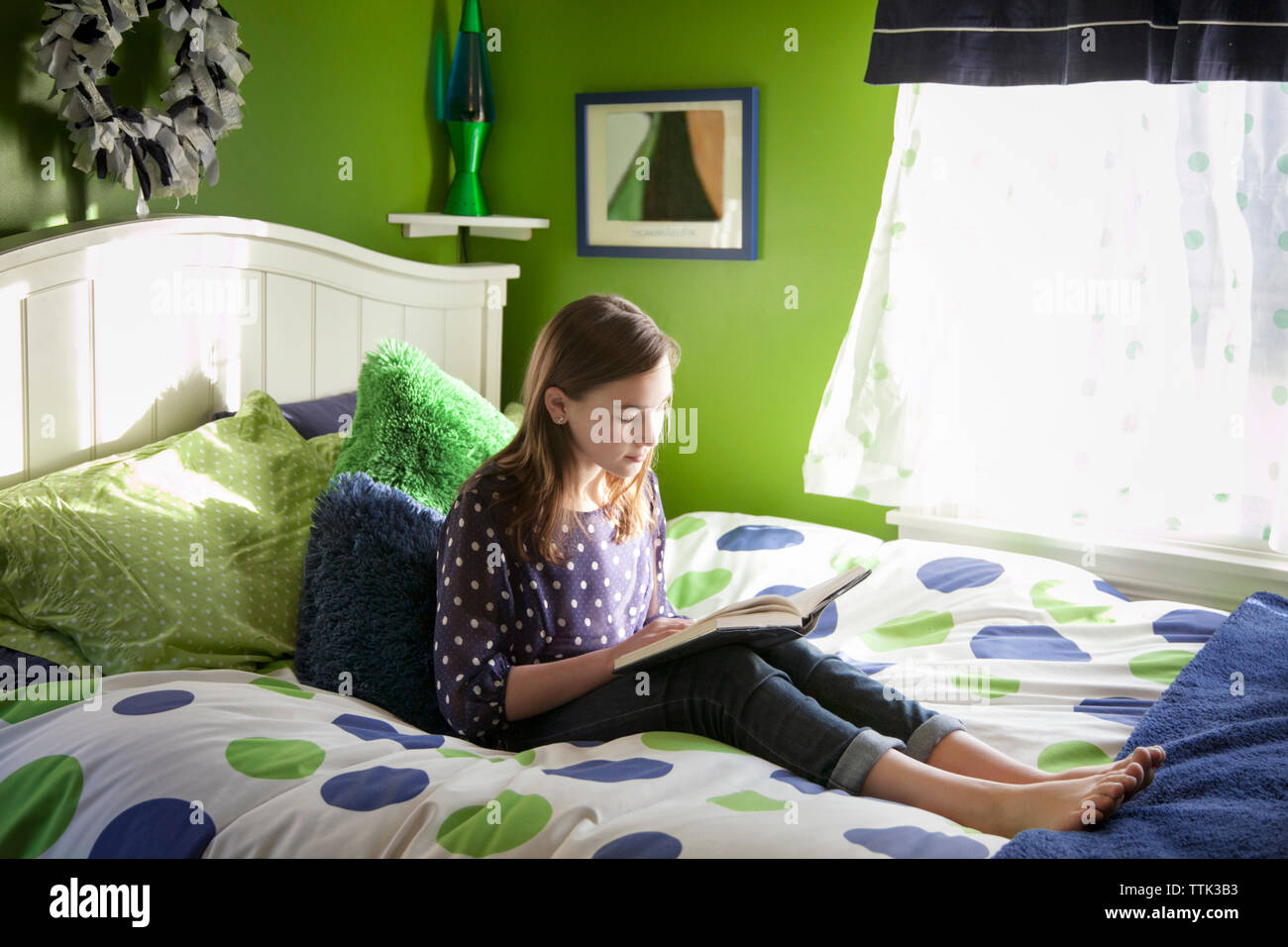 Lettura della ragazza prenota comodamente seduti sul letto di casa Foto Stock