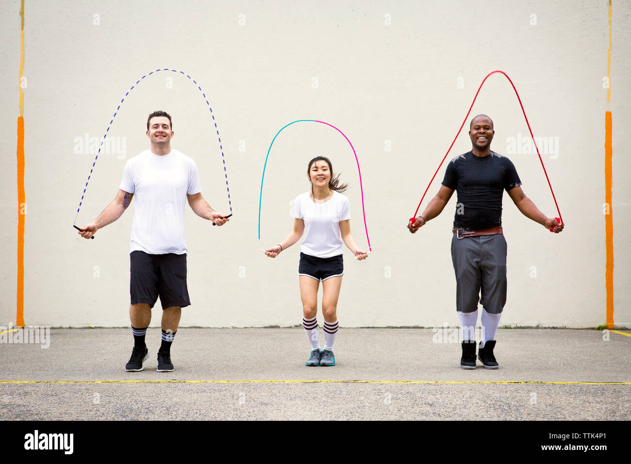 Happy amici a giocare con jump corde sulla strada contro la parete Foto Stock