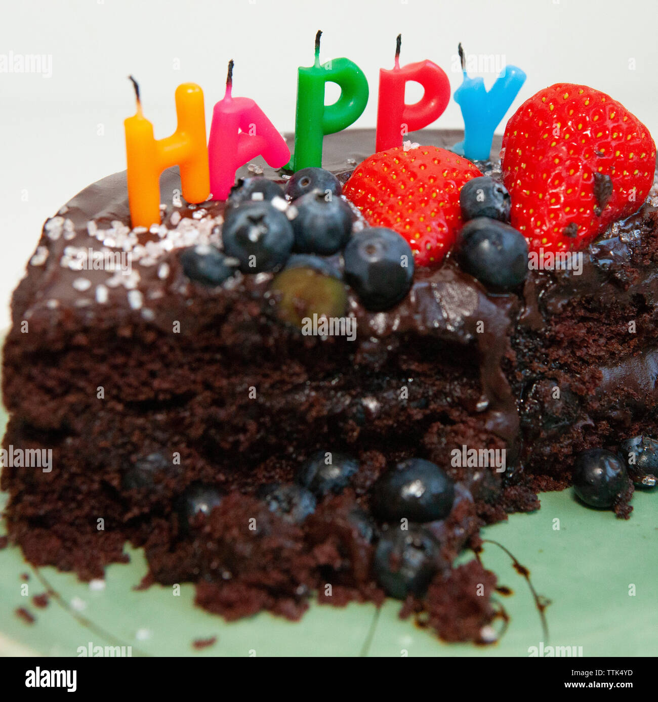 Un parzialmente mangiato torta al cioccolato con soffiato-out candele dicendo felice. La torta è decorata con mirtilli e fragole, glassa di cioccolato e rosa s Foto Stock
