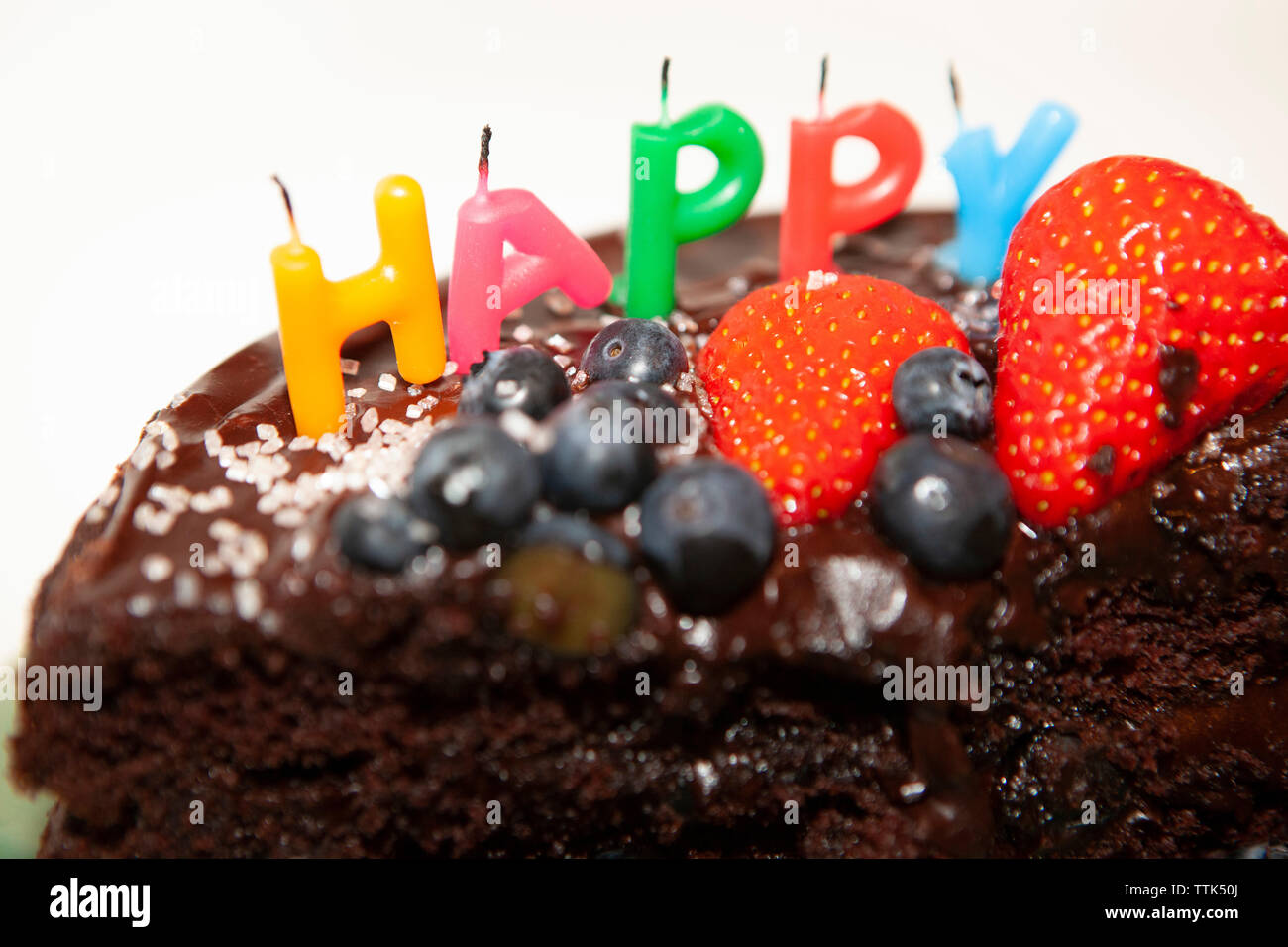Un parzialmente mangiato torta al cioccolato con soffiato-out candele dicendo felice. La torta è decorata con mirtilli e fragole, glassa di cioccolato e rosa s Foto Stock