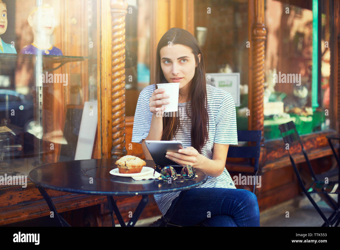 Donna di bere il caffè tenendo tavoletta digitale e seduti al cafè sul marciapiede Foto Stock