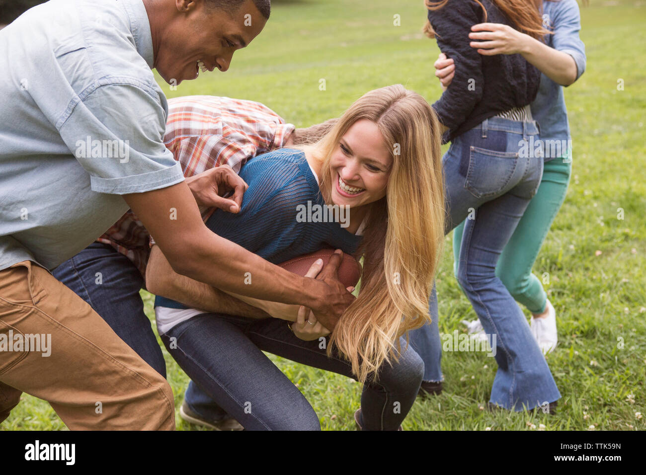 Amici maschi strappi palla calcio da donna sul campo erboso Foto Stock