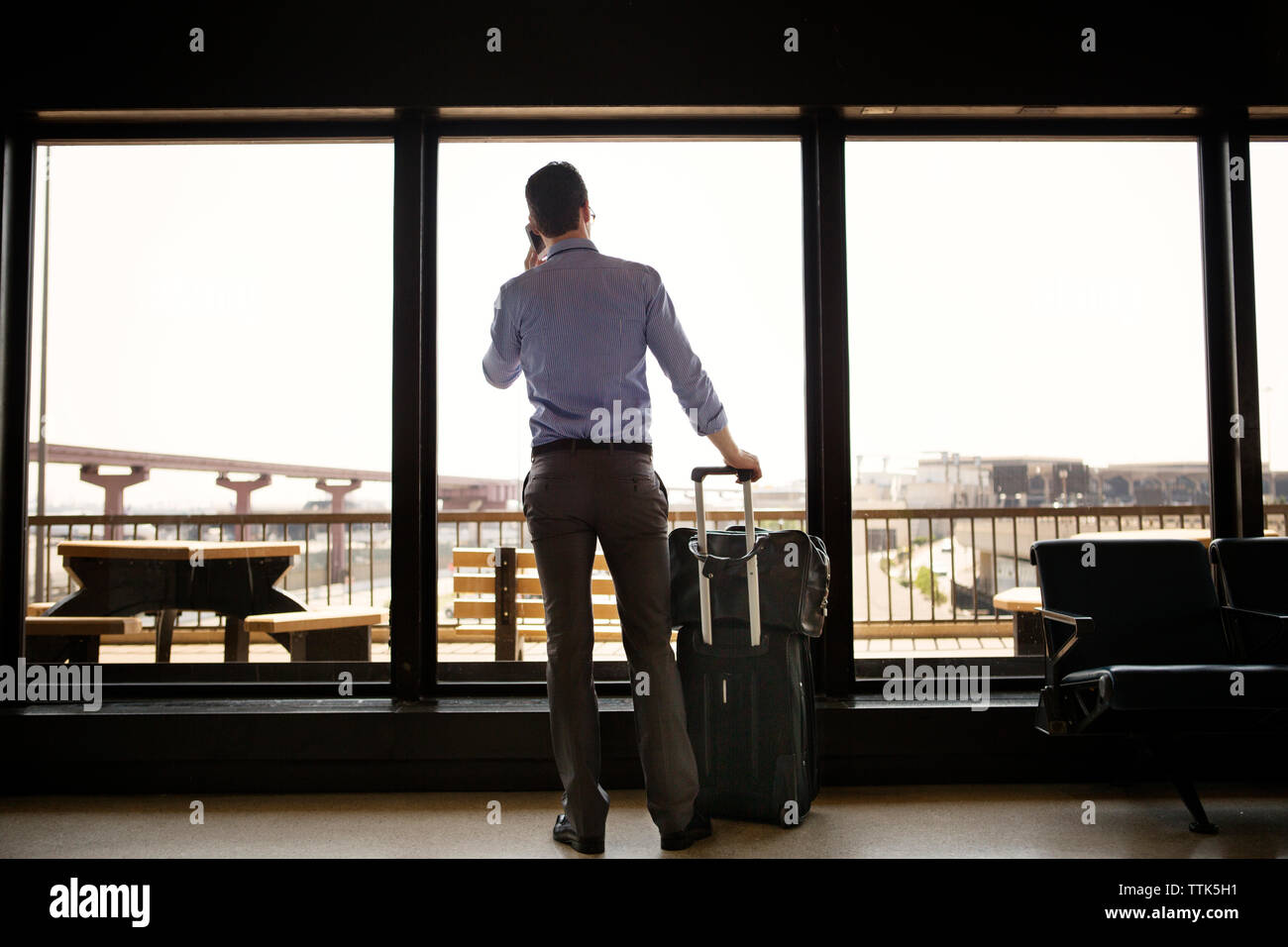 Vista posteriore di imprenditore rispondere alle chiamate mentre in piedi contro la finestra alla stazione della metropolitana Foto Stock