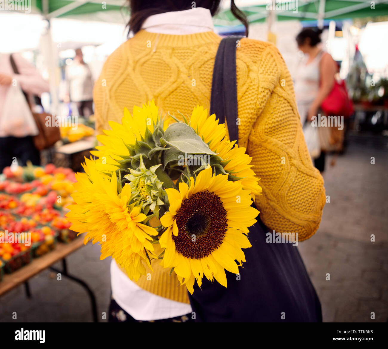 Vista posteriore della donna che la porta di girasoli in borsa sul mercato Foto Stock