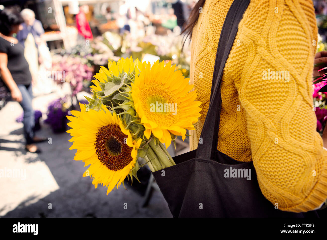 Sezione mediana della donna che la porta di girasoli in borsa sul mercato Foto Stock