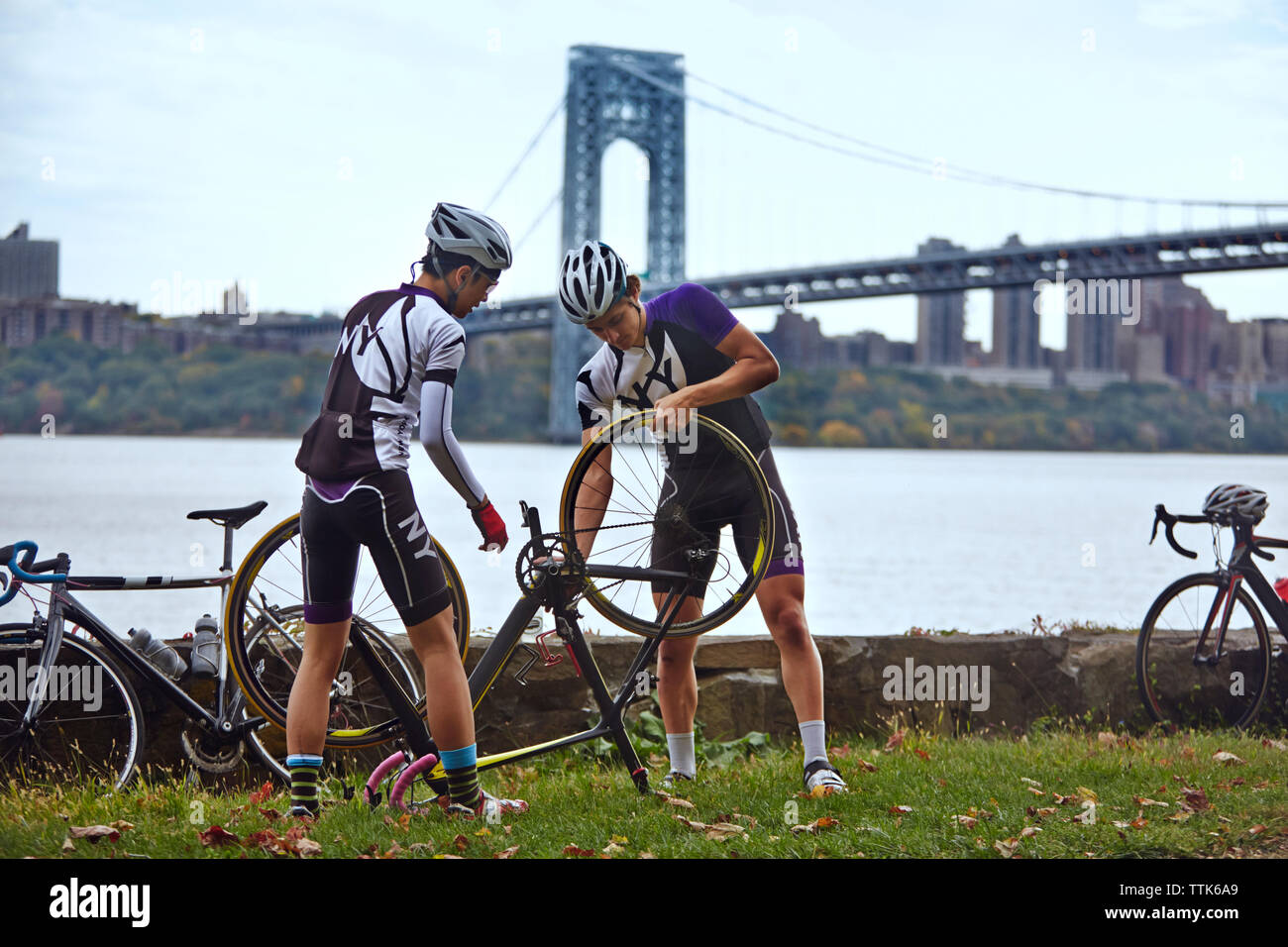Gli atleti di sesso maschile riparazione bicicletta contro George Washington Bridge Foto Stock
