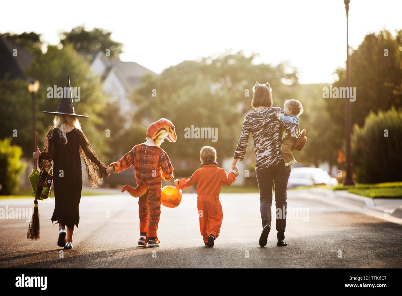 Vista posteriore delle donne con bambini vestiti per la festa di Halloween camminando sulla strada Foto Stock