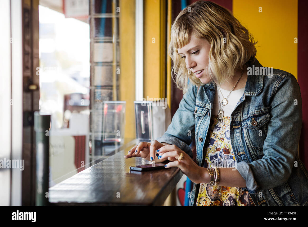 Donna che utilizza smart phone dalla finestra nel cafe Foto Stock
