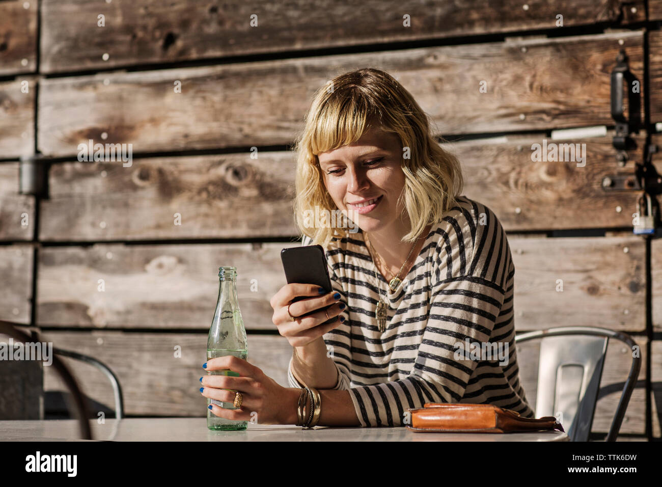 Donna che utilizza smart phone tenendo bottiglia di soda in cafe Foto Stock