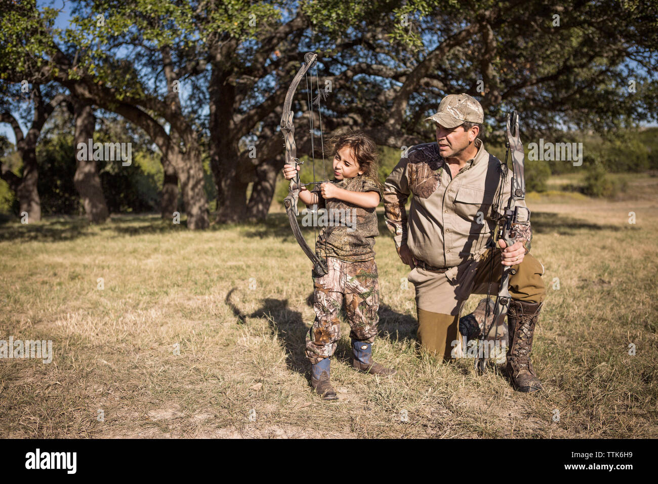 Ragazza mirando con la freccia mentre padre guida su campo erboso Foto Stock