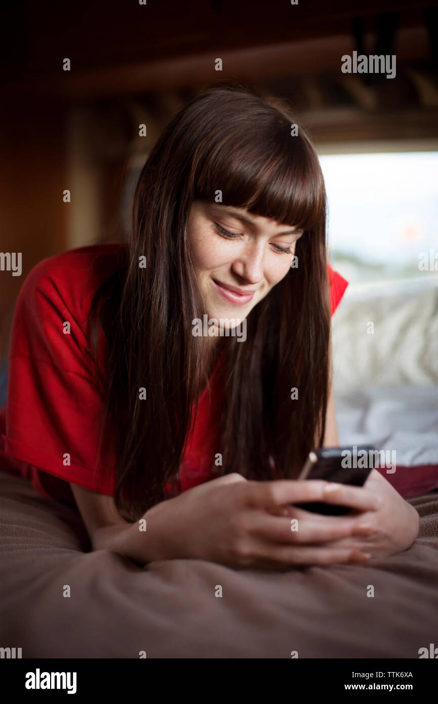 Donna felice utilizzando smart phone mentre vi rilassate sul letto in camper Foto Stock