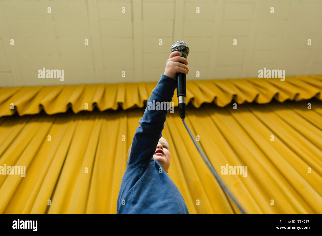 Basso angolo vista del ragazzo tenendo il microfono allo stadio contro tende gialle Foto Stock