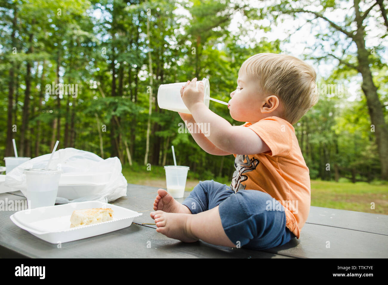 Lunghezza completa di simpatici baby boy bere drink seduto sulla tavoletta picnic al parco Foto Stock
