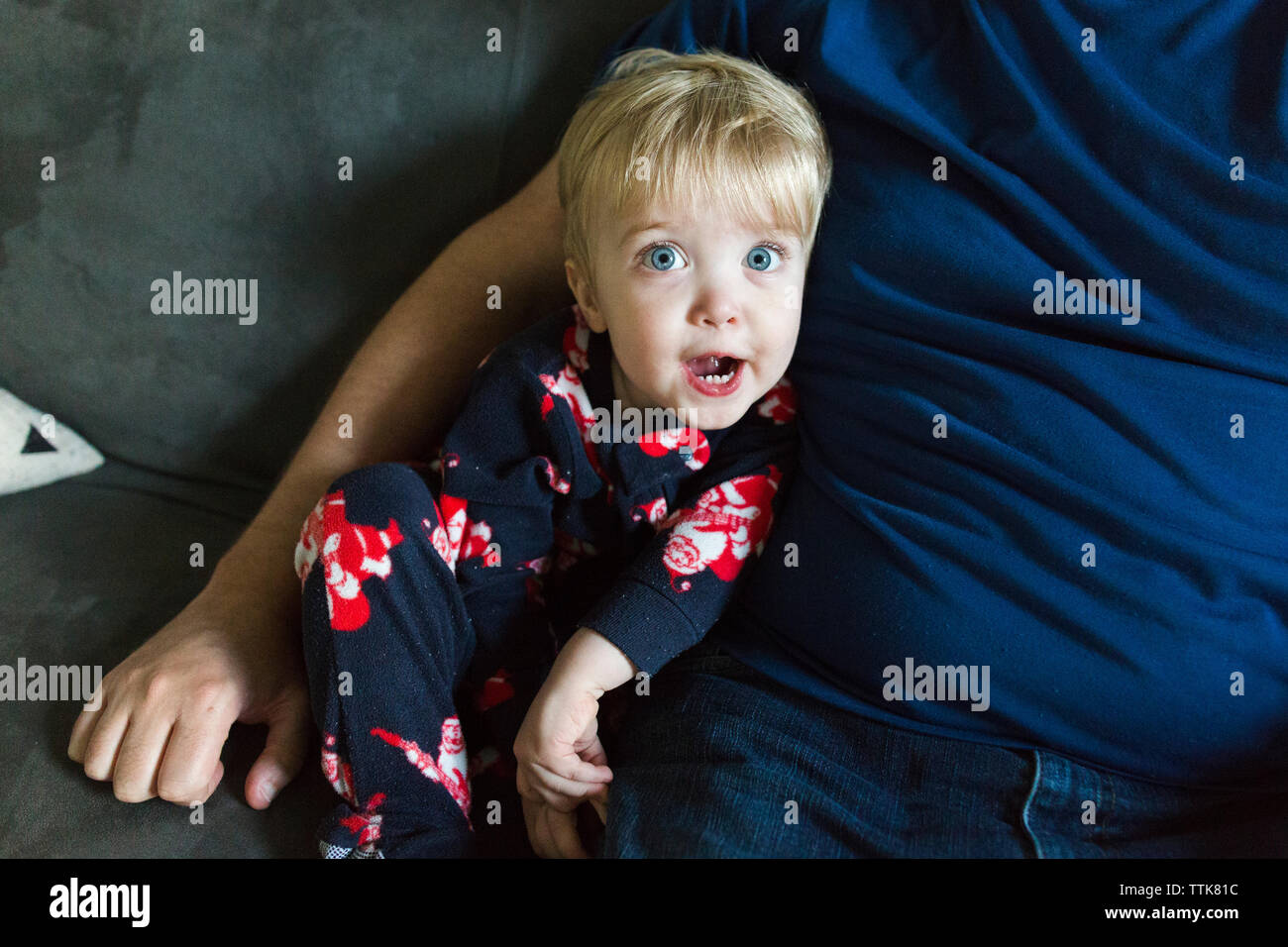 Il Toddler boy sembra sorpreso mentre è seduto accanto a papà Foto Stock